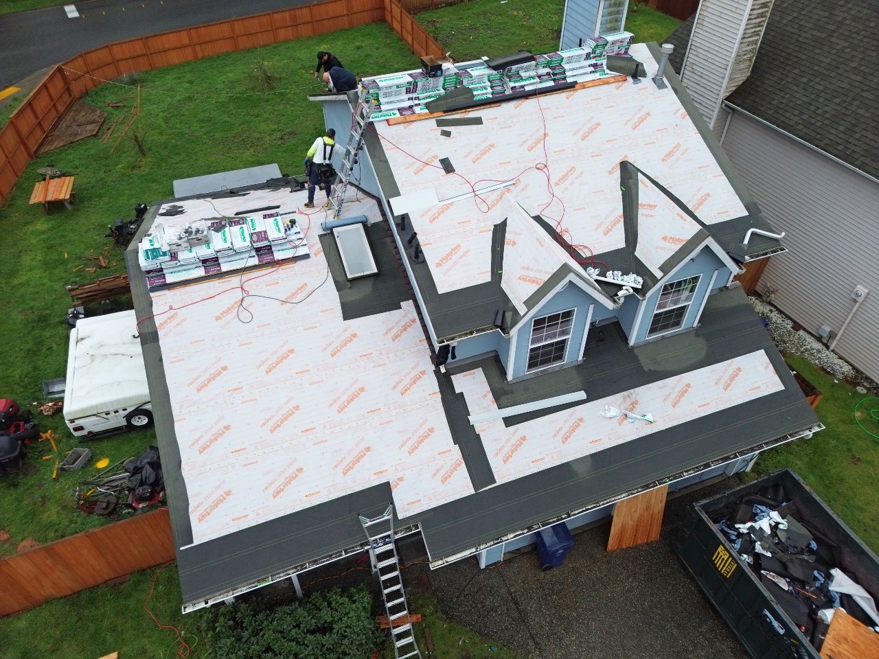 Roof replacement in progress, synthetic underlayment installed on a home with blue dormers